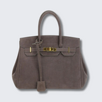 Sac à main en cuir marron avec fermoir doré, style Birkin, sur fond gris clair. Accessoire de mode élégant et luxueux pour femme.