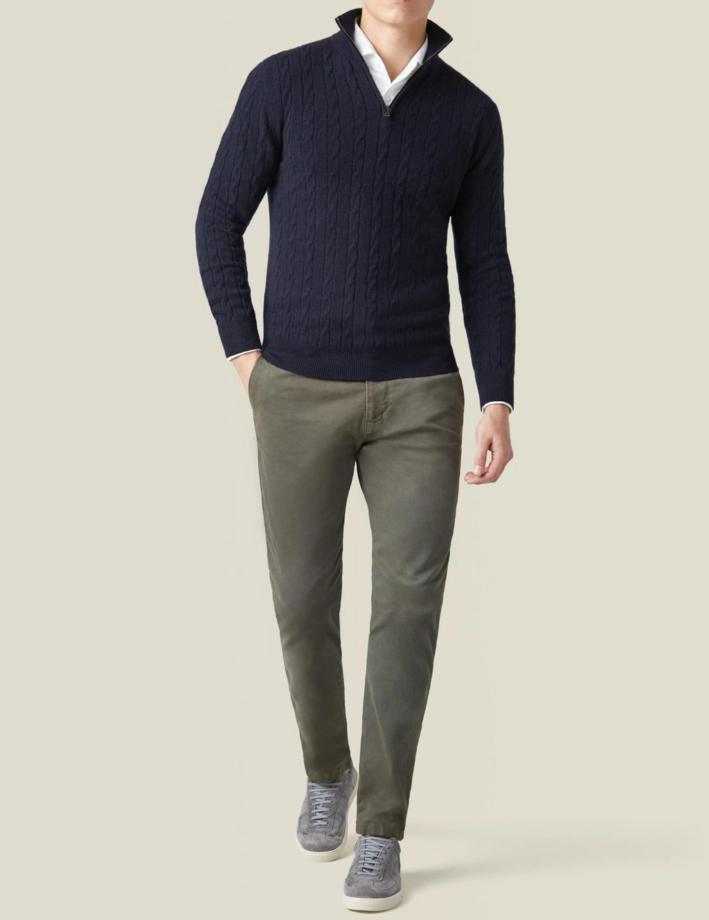 Homme portant un pull bleu marine à col zippé, pantalon kaki et baskets grises. Mode masculine élégante, tenue décontractée chic.