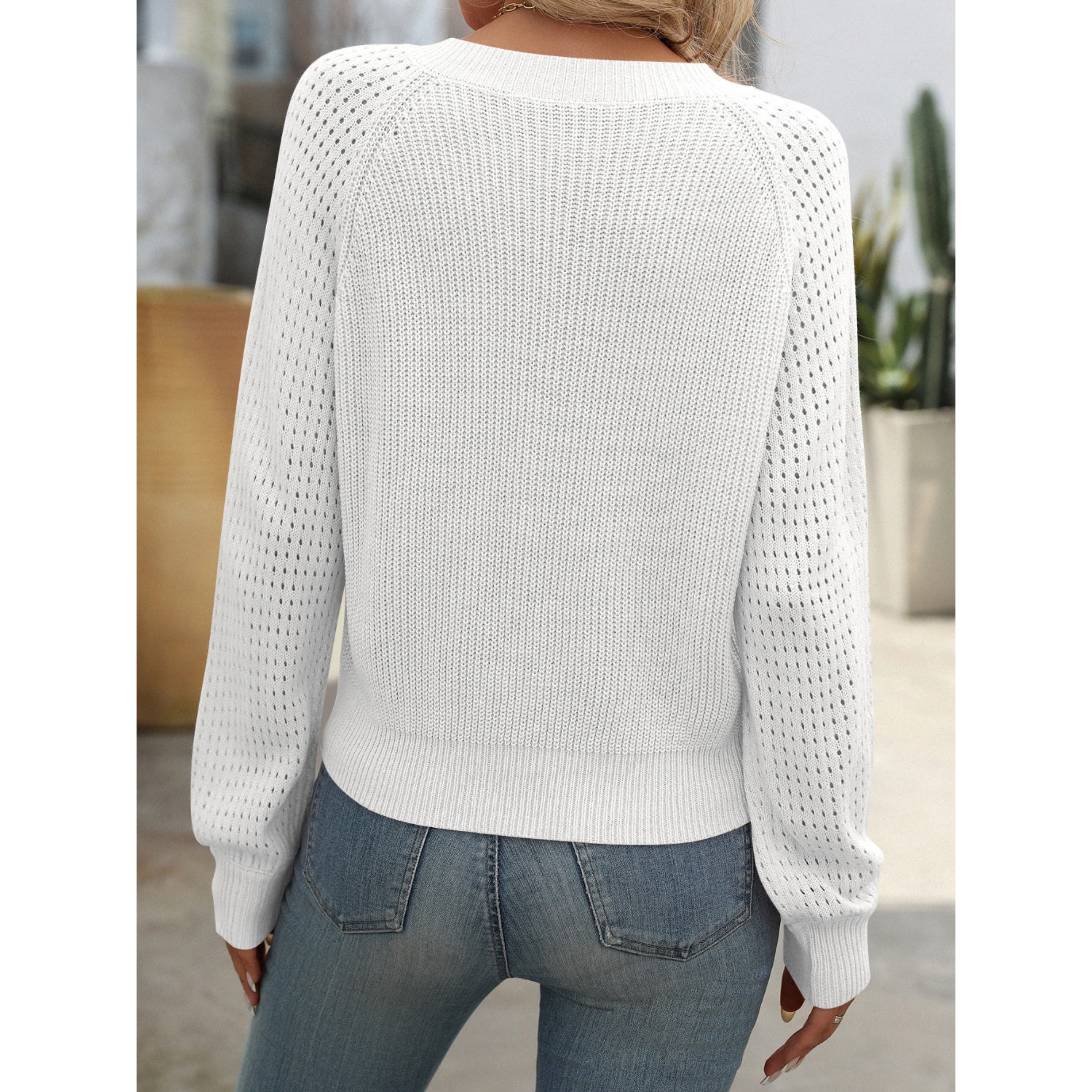 Femme portant un pull blanc en tricot ajouré, manches longues, dos visible, avec un jean bleu. Mode décontractée, style automne-hiver.