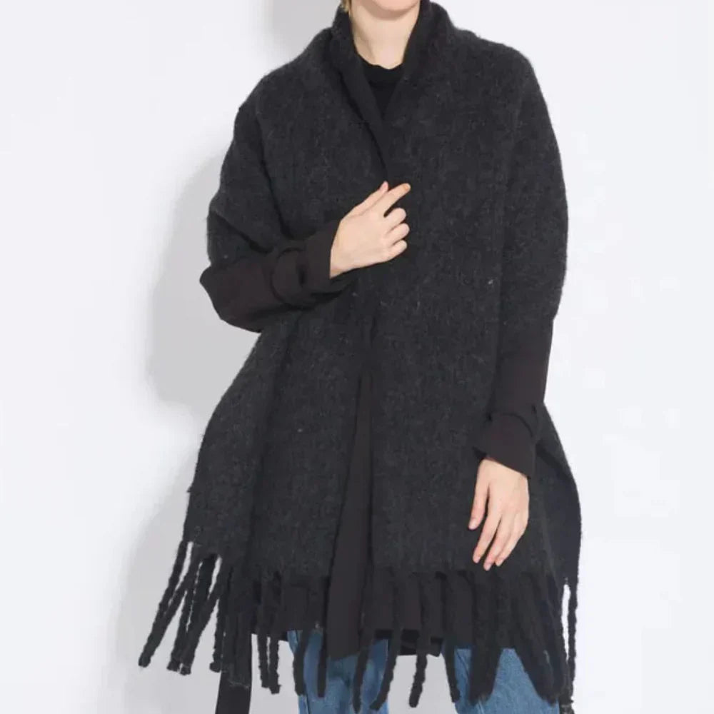 Femme portant un poncho noir en laine avec franges, style décontracté, sur fond blanc. Mode automne-hiver, vêtement chaud et élégant.