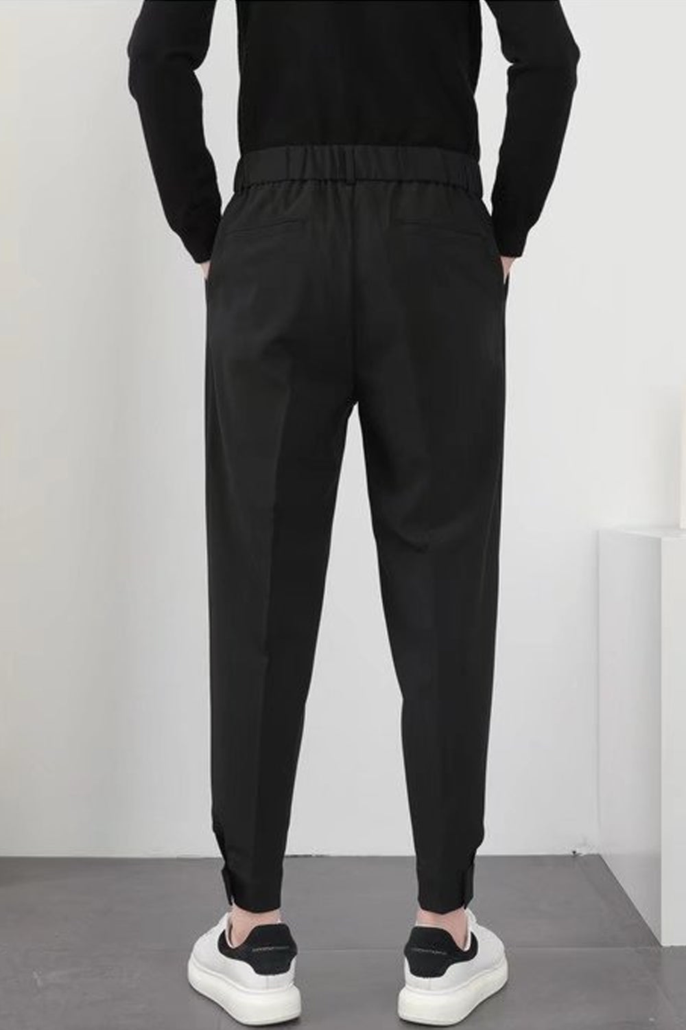 Homme en pantalon noir élégant, vue de dos, portant des baskets blanches. Mode masculine moderne, style décontracté chic.