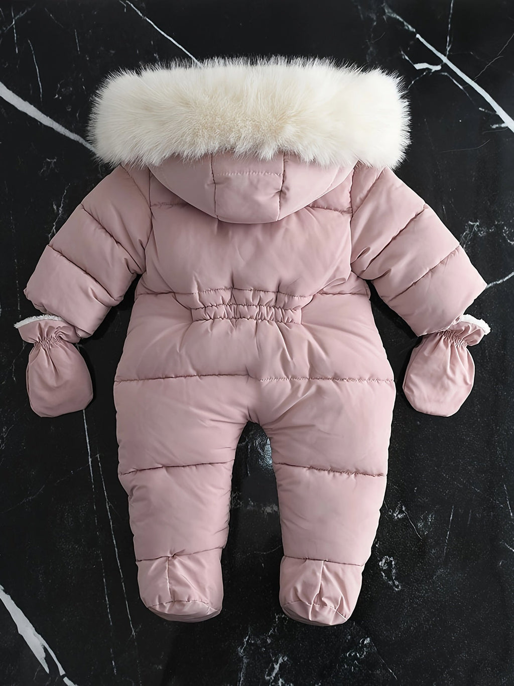 Combinaison bébé rose avec capuche bordée de fourrure blanche, gants assortis, sur fond marbré noir. Vêtement d'hiver chaud et élégant.