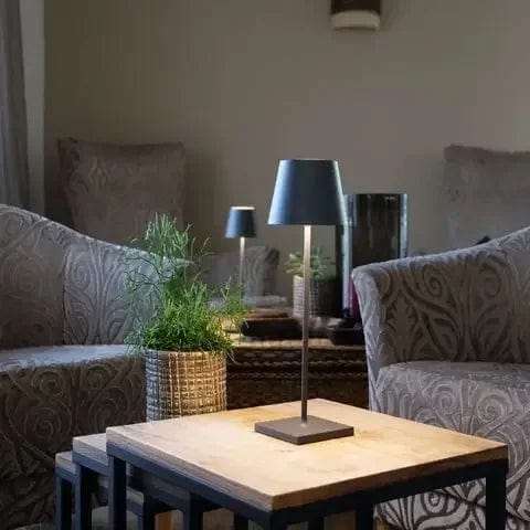 Lampe de table moderne sur une table en bois, entourée de fauteuils élégants et de plantes vertes, créant une ambiance cosy et contemporaine.