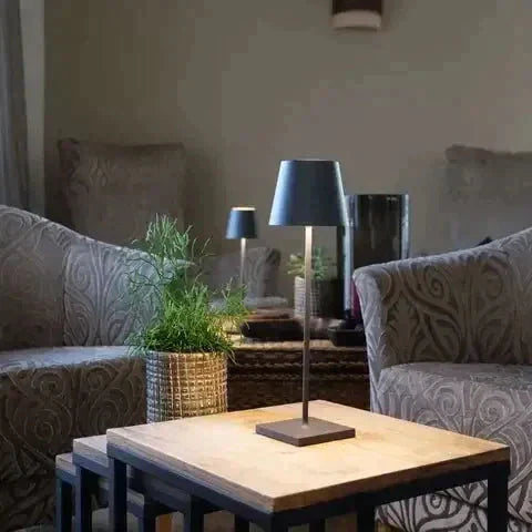 Lampe de table moderne sur une table en bois entre deux fauteuils élégants, décorée avec une plante verte, créant une ambiance chaleureuse et sophistiquée.