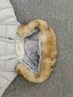 Doudoune grise avec capuche en fausse fourrure marron, posée sur un tapis gris. Veste chaude hiver, mode femme, tendance.