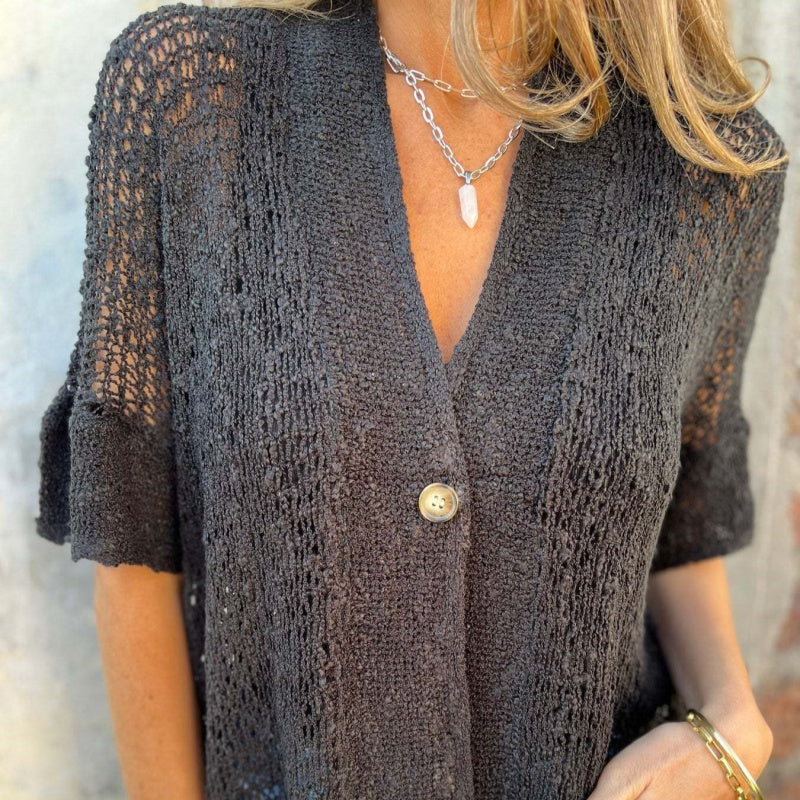 Femme portant un cardigan en maille noire avec bouton unique, collier en chaîne argentée et pendentif, style décontracté chic, mode automne.