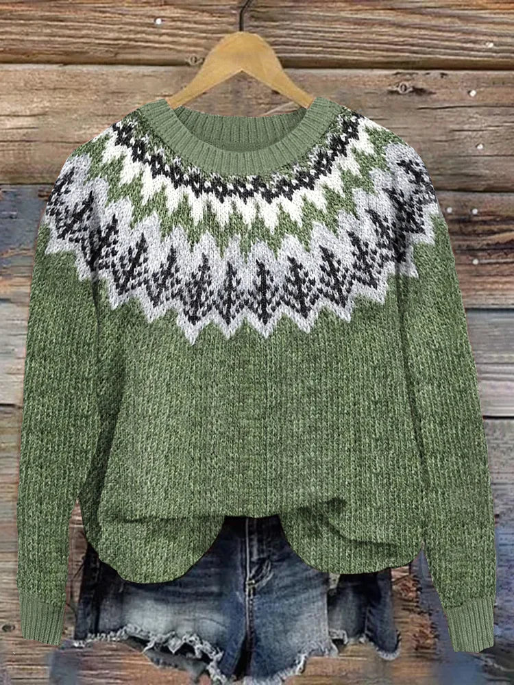 Pull-over vert à motifs nordiques noirs et blancs, suspendu sur un cintre en bois, avec un short en jean délavé en arrière-plan sur fond de bois.