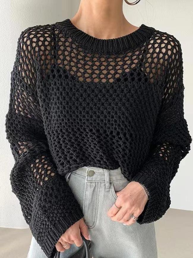 Femme portant un pull en maille noire ajourée, manches longues, avec un jean taille haute gris. Mode automne, style décontracté chic.