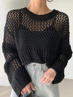 Femme portant un pull en maille noire ajourée, manches longues, avec un jean taille haute gris. Mode automne, style décontracté chic.