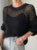 Pull en maille noire ajourée, manches longues, porté avec un jean gris clair. Mode automne, style décontracté, tendance tricot femme.
