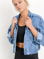 Femme portant une veste en jean bleu sur un haut noir, posant contre un fond blanc. Mode décontractée, style moderne, tenue tendance.