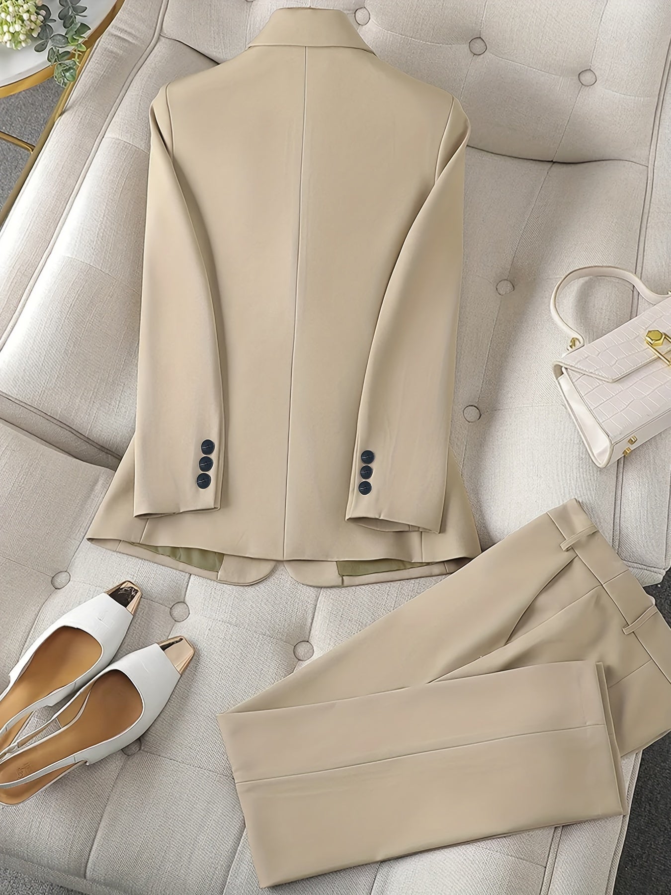 Costume beige élégant sur un canapé, accompagné de chaussures blanches à talons et d'un sac à main blanc. Mode chic, tenue formelle pour femmes.