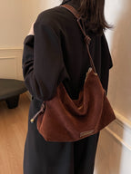 Femme en manteau noir portant un sac à main en daim marron, style élégant et moderne, intérieur minimaliste, mode automne-hiver tendance.