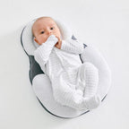 Bébé allongé sur un coussin ergonomique blanc, vêtu d'un pyjama rayé gris, sur fond blanc. Confort, sécurité, sommeil bébé.