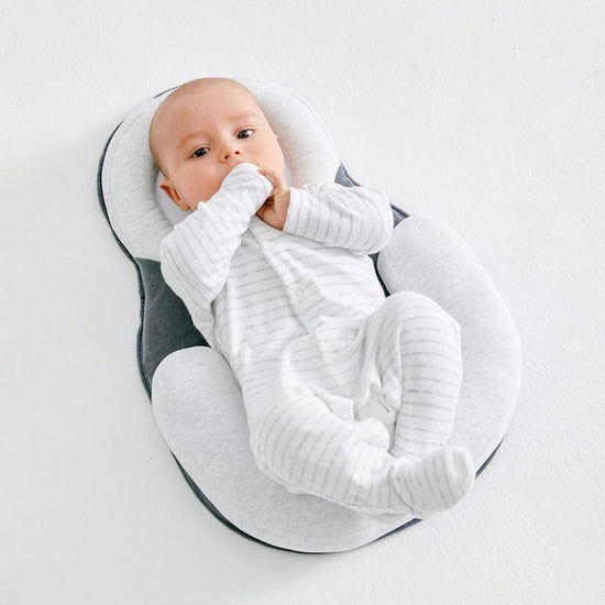 Bébé allongé sur un coussin ergonomique blanc, vêtu d'un pyjama rayé gris, sur fond blanc. Confort, sécurité, sommeil bébé.
