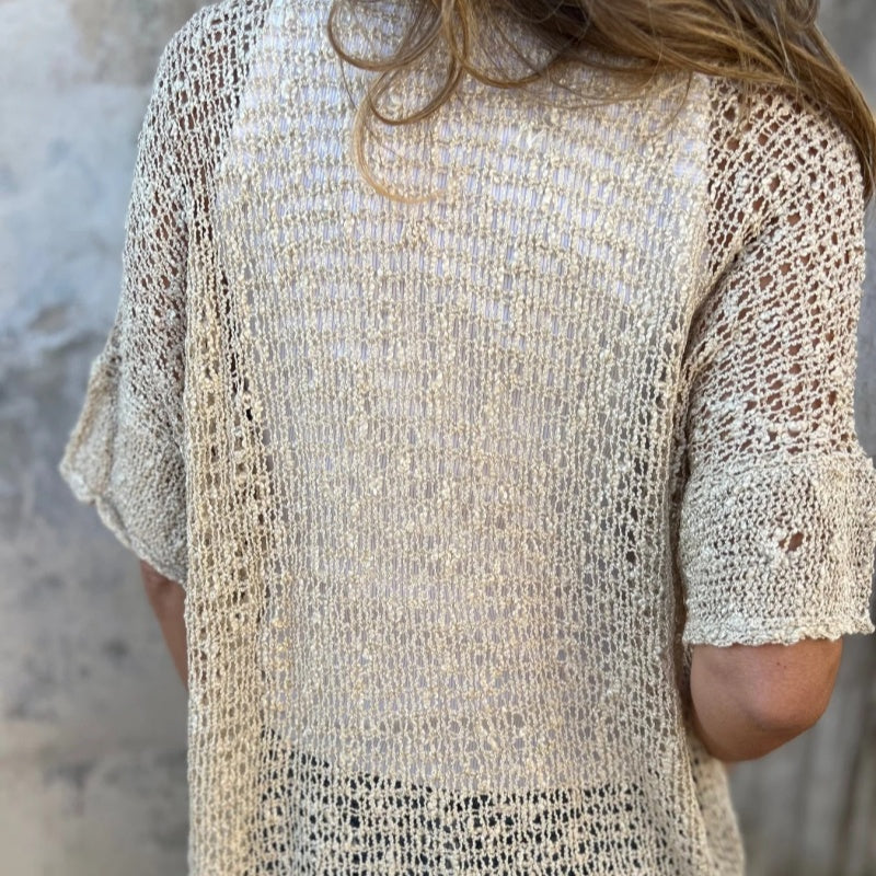 Femme portant un pull en maille beige, dos visible, texture ajourée. Mode éco-responsable, tendance tricot, style décontracté.