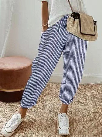 Femme portant un pantalon rayé bleu et blanc, t-shirt blanc, baskets blanches et sac en paille. Mode décontractée, style estival, tenue confortable.