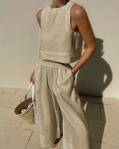 Femme en tenue estivale beige, portant un ensemble en lin avec un top sans manches et un pantalon ample, tenant un sac en osier.