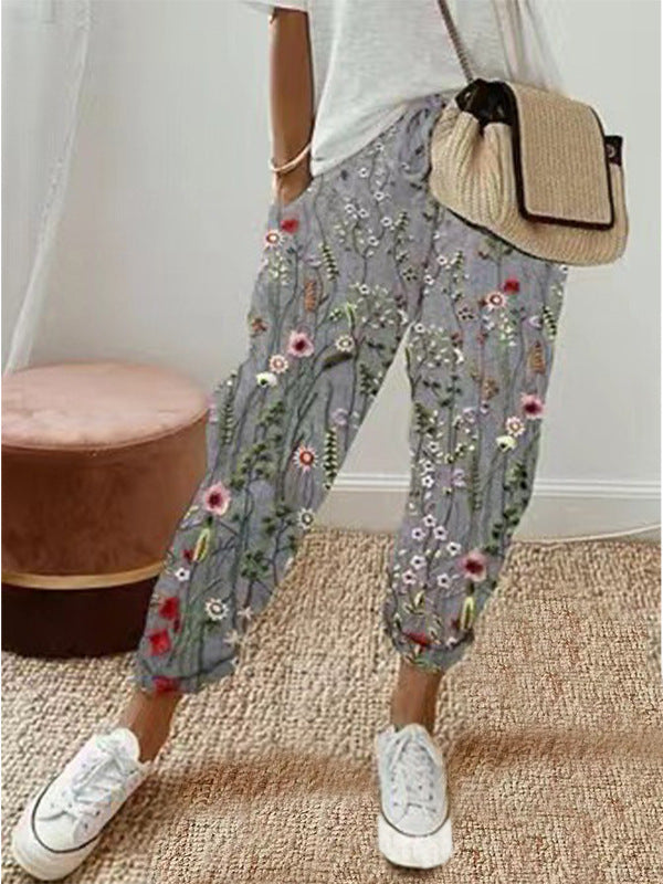 Pantalon femme à motifs floraux colorés, porté avec un t-shirt blanc et un sac à main beige. Style décontracté et tendance pour l'été.