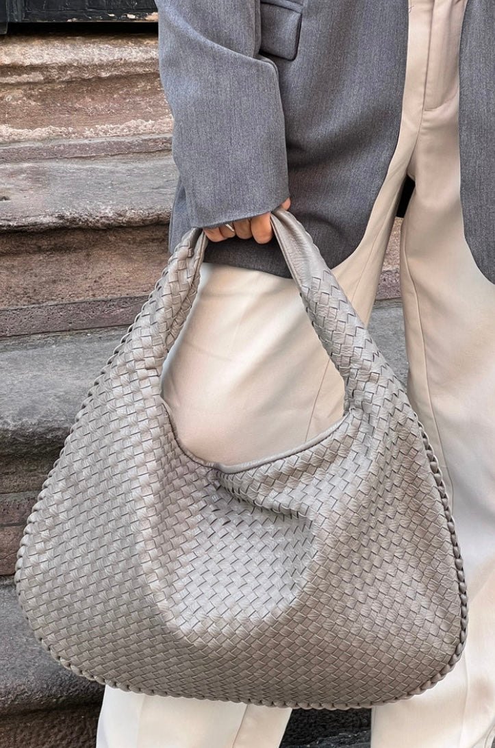 Sac à main tissé gris argenté porté par une personne en pantalon blanc et veste grise, mode élégante et tendance, accessoire chic pour femme.