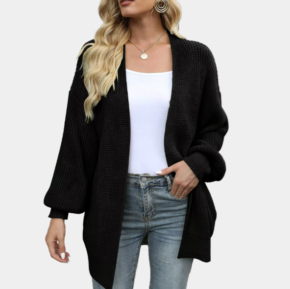 Femme portant un cardigan noir ample, t-shirt blanc et jeans, style décontracté chic, mode automne-hiver, accessoires dorés, cheveux ondulés.