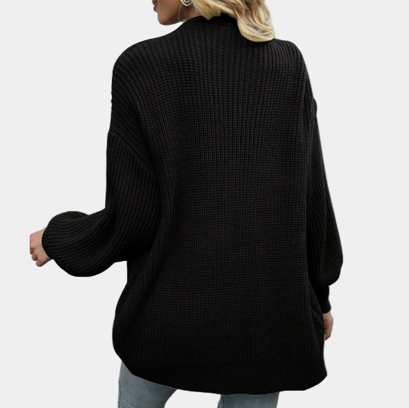 Femme portant un pull oversize noir en maille, manches longues, sur fond blanc. Mode automne-hiver, style décontracté et tendance.
