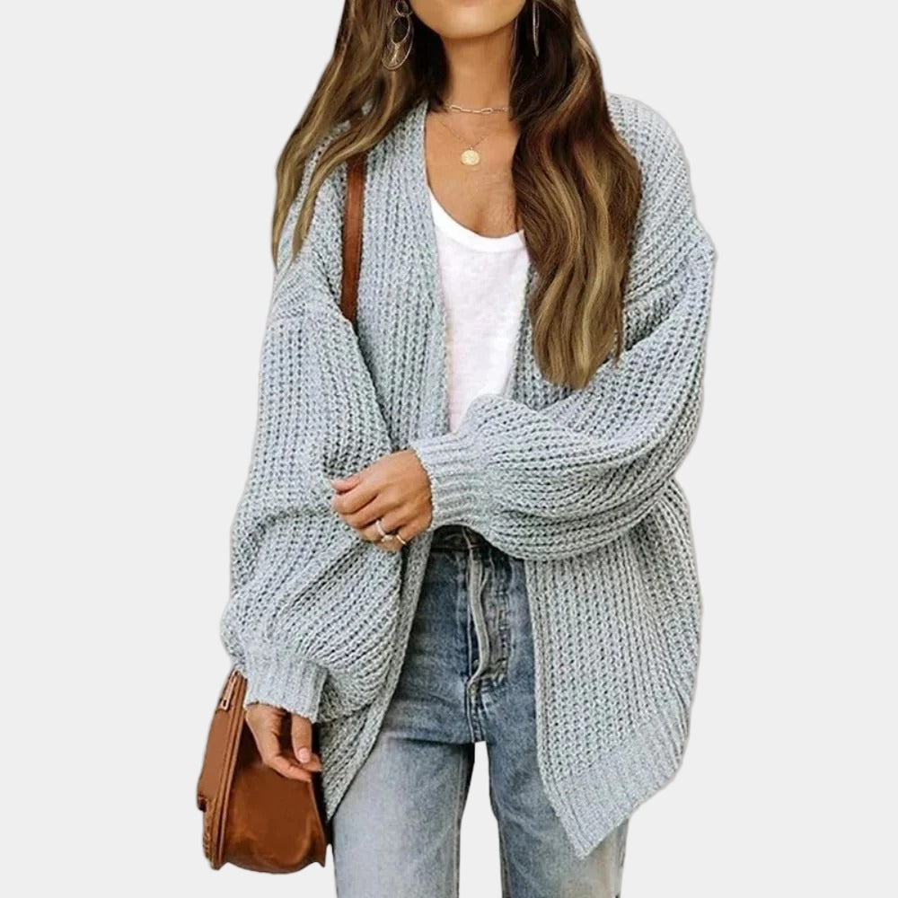 Femme portant un cardigan en maille gris, t-shirt blanc, jean bleu et sac marron. Mode automne, style décontracté, tenue tendance.