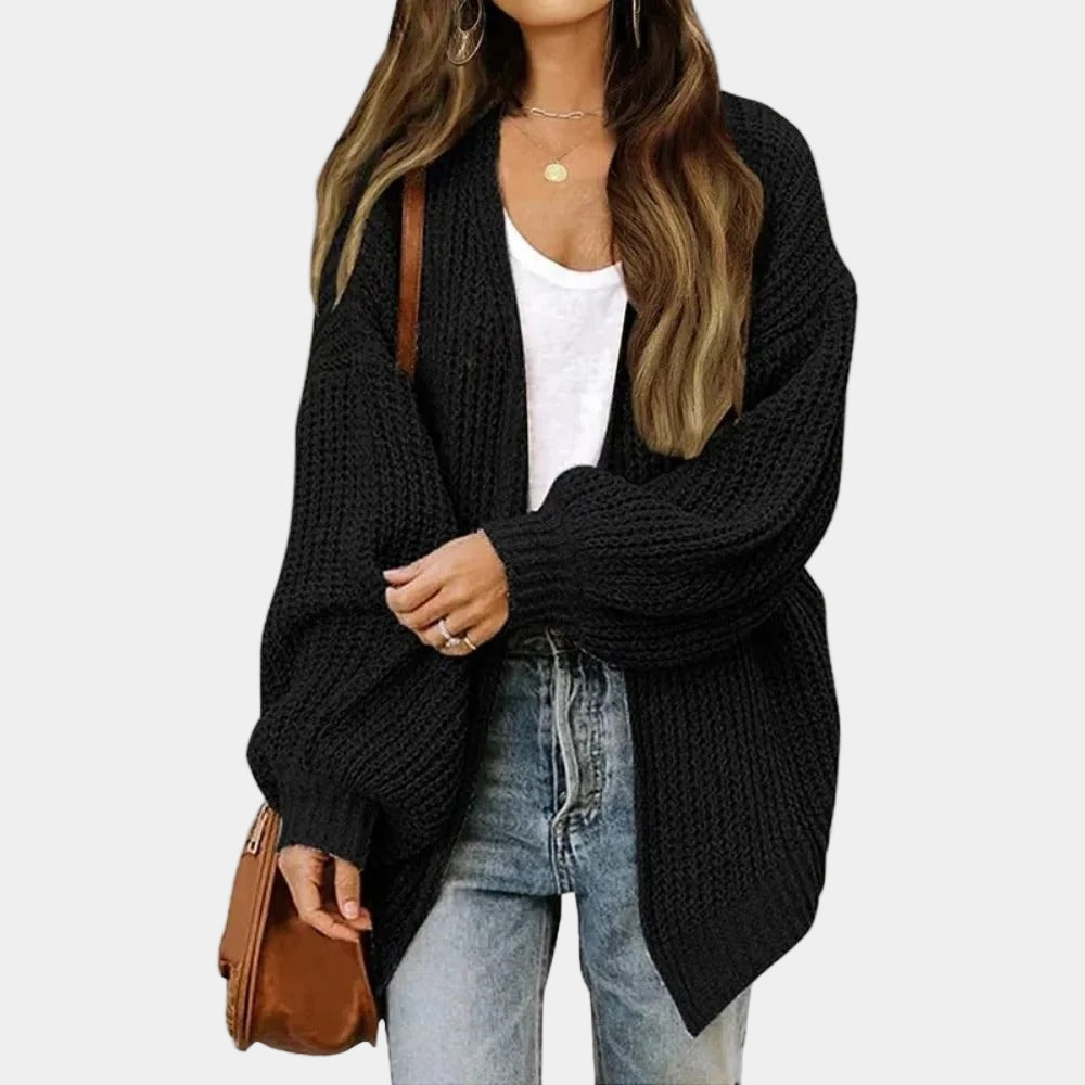 Femme portant un cardigan noir en maille, t-shirt blanc, jean décontracté et sac marron. Mode automne, style décontracté, tenue élégante.
