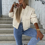 Femme en veste beige tendance, posant sur des escaliers en béton, portant un jean bleu et une montre dorée, style urbain chic.
