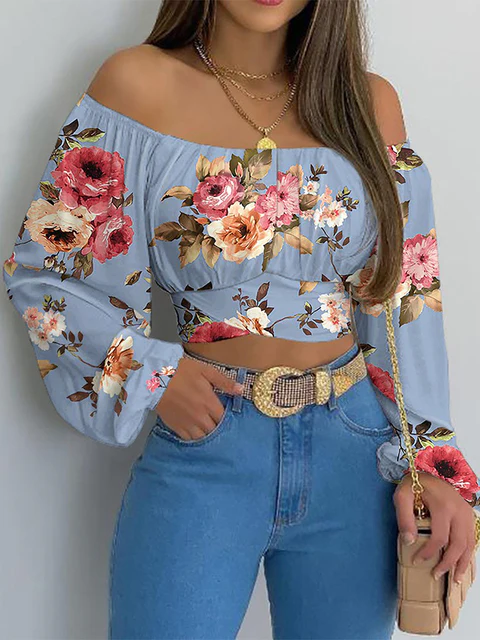 Femme portant un haut à épaules dénudées bleu à motifs floraux, jeans taille haute, ceinture dorée, collier en chaîne et sac beige. Mode tendance.