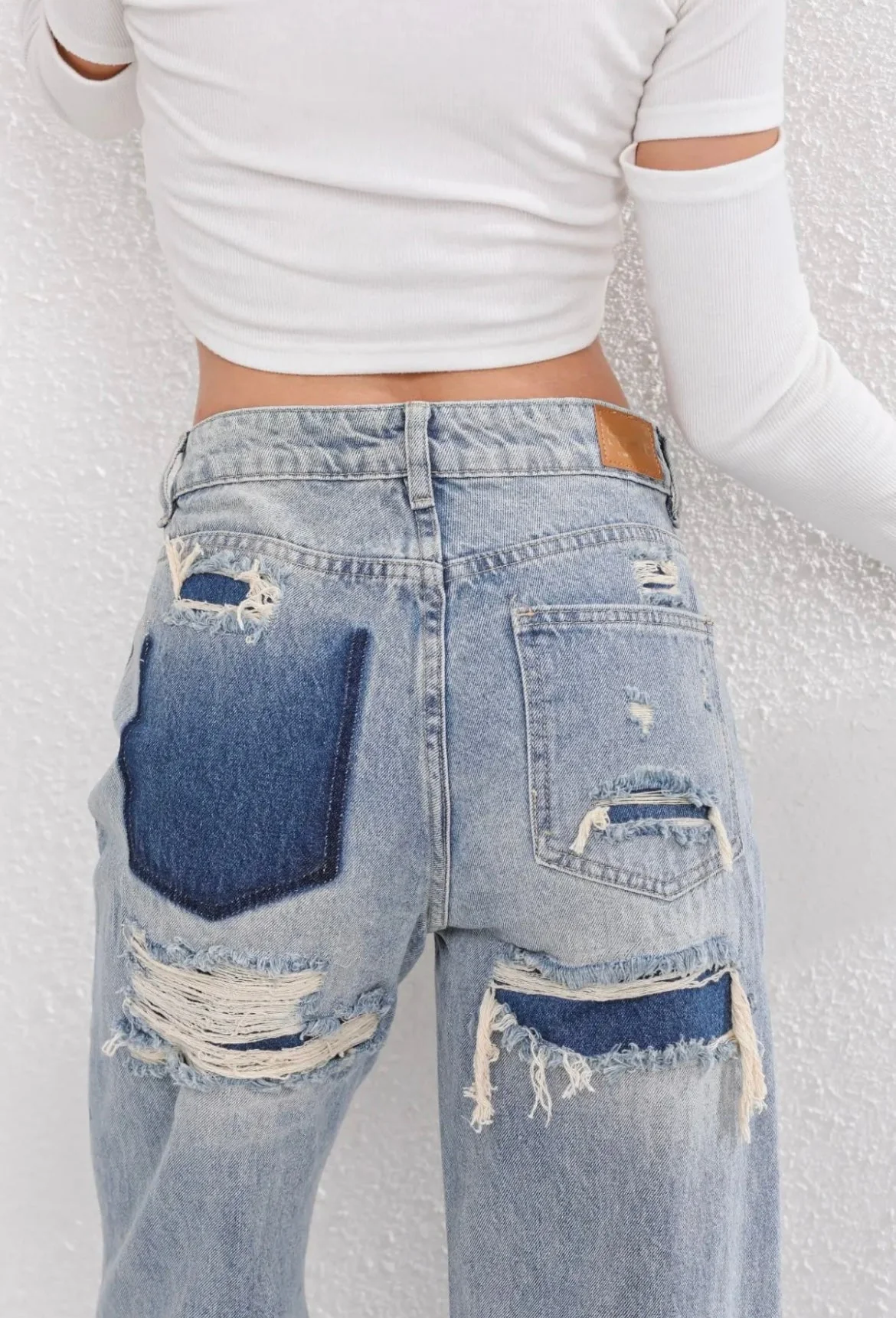 Jeans déchirés tendance avec poches arrière contrastées, portés par une femme en haut blanc. Mode urbaine, style décontracté, denim vintage.