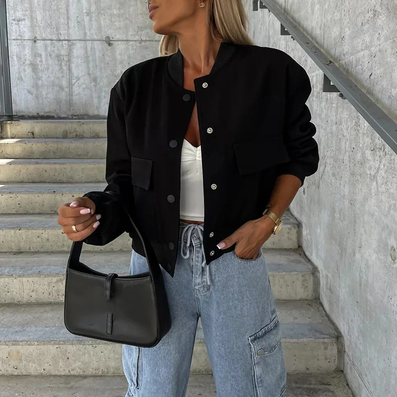 Femme en veste noire, top blanc et jean cargo, tenant un sac à main noir. Mode urbaine, style décontracté, escalier en béton en arrière-plan.