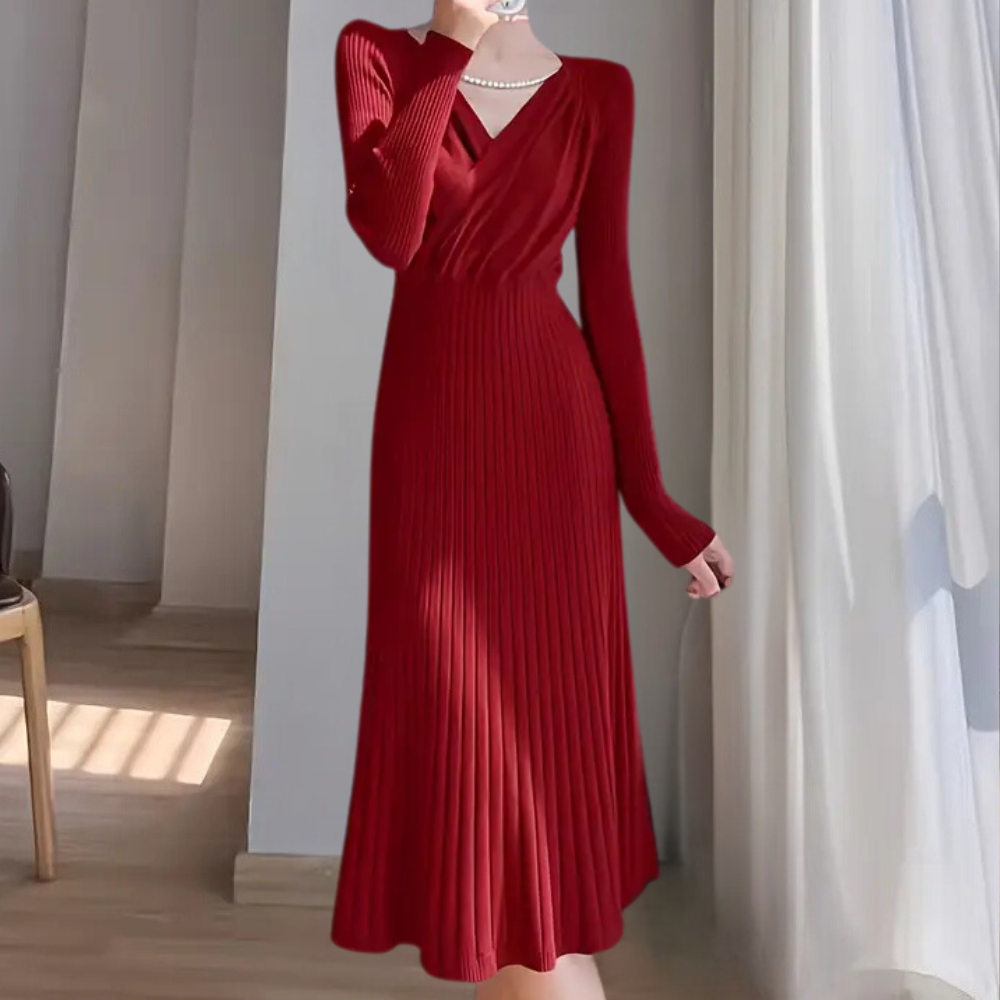 Robe rouge élégante à manches longues, col en V, plissée, portée par une femme près d'une fenêtre lumineuse. Mode féminine chic et moderne.