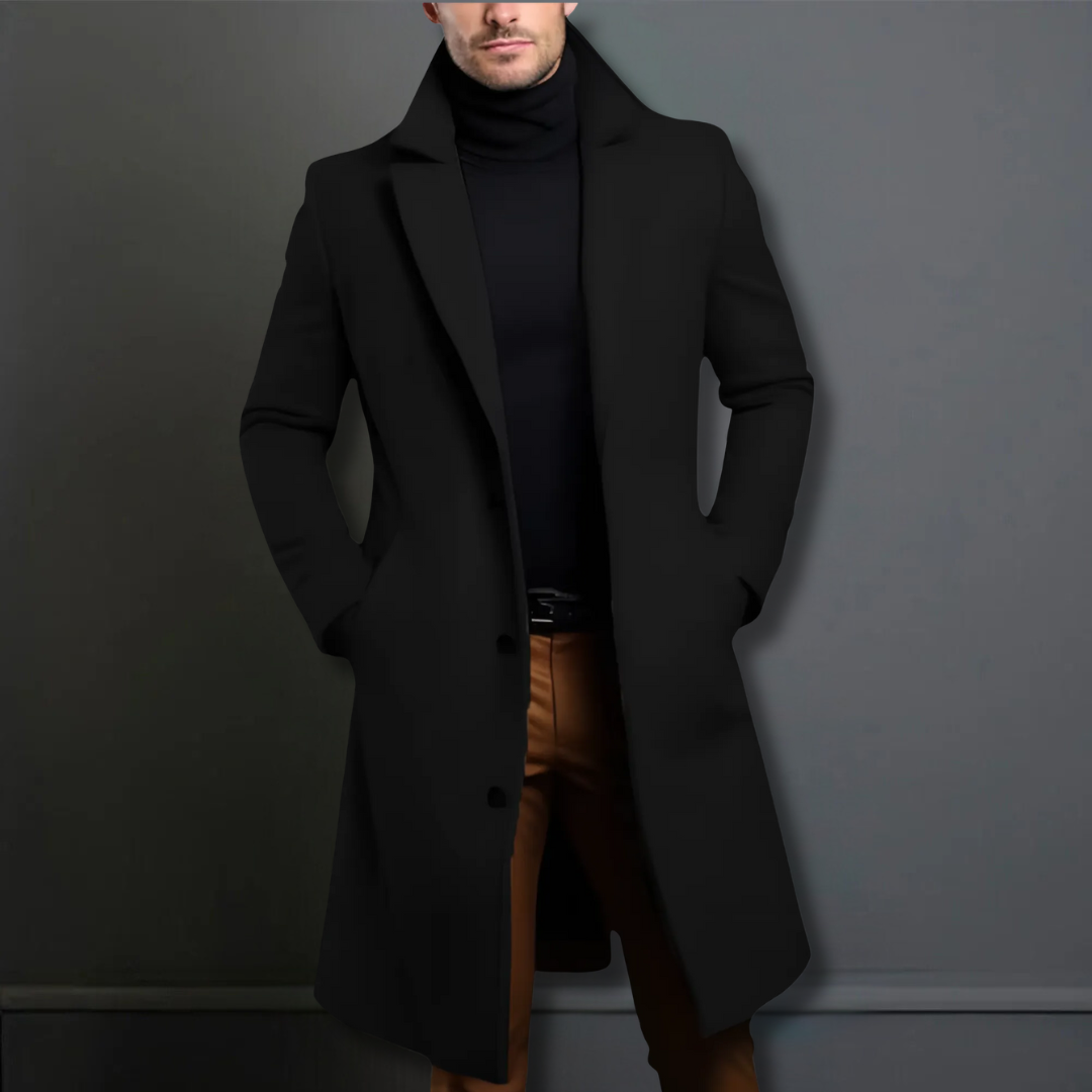 Homme portant un manteau noir élégant, col relevé, sur un pull noir et un pantalon marron. Mode masculine chic, style automne-hiver.