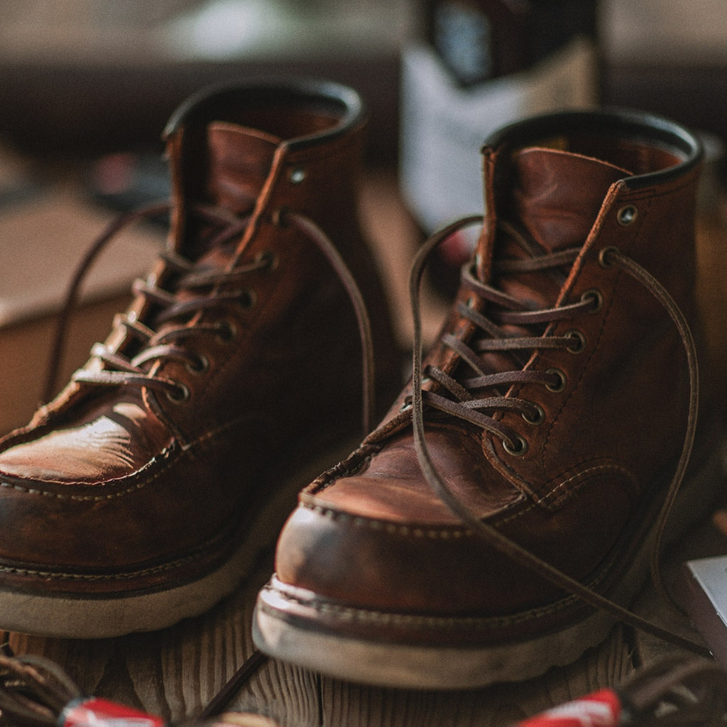 Chaussures en cuir marron vintage sur une table en bois, lacets défaits, ambiance rétro. Accessoires de mode homme, style classique et robuste.