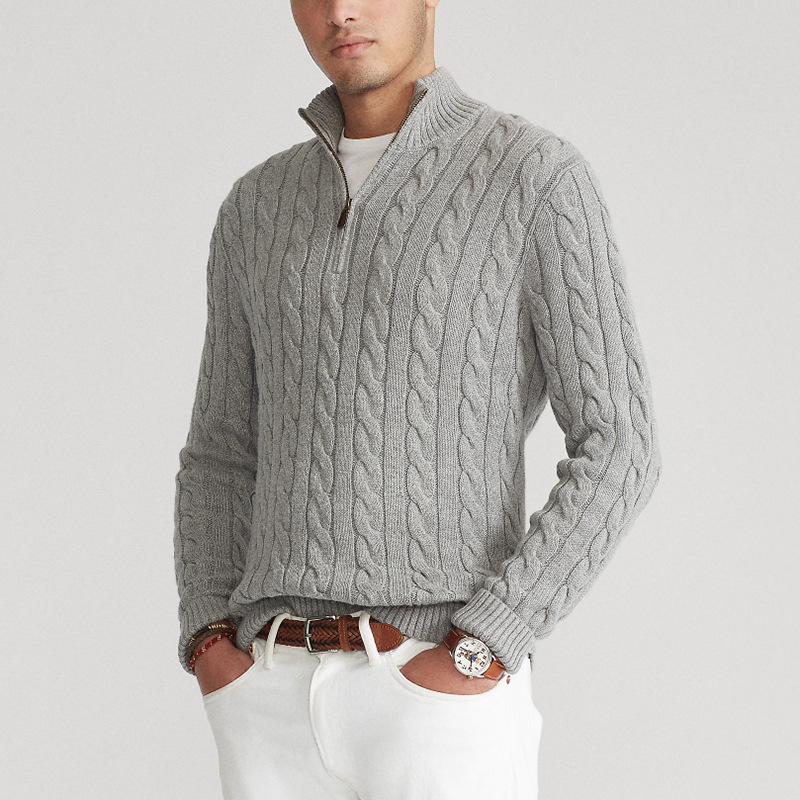 Homme portant un pull torsadé gris avec col zippé, associé à un pantalon blanc. Mode masculine élégante, tenue automne-hiver tendance.