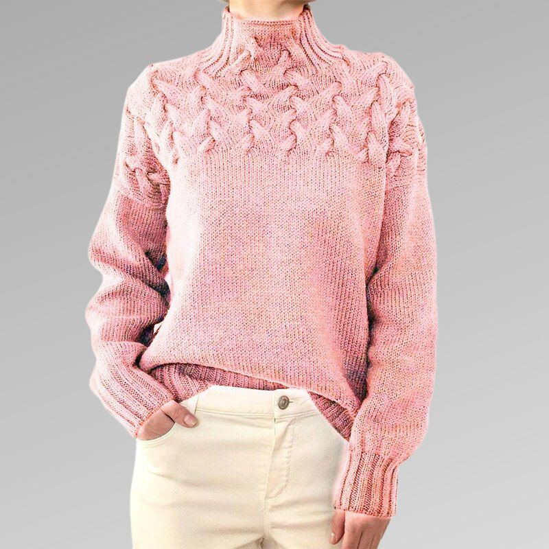 Pull rose en laine torsadée, manches longues, col montant, porté avec un pantalon blanc. Mode hiver, style décontracté et élégant.