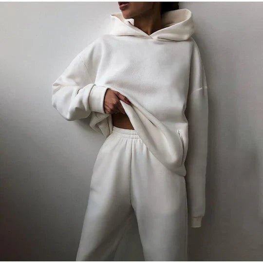 Personne portant un ensemble de survêtement blanc, composé d'un sweat à capuche et d'un pantalon confortable. Mode décontractée, style minimaliste.