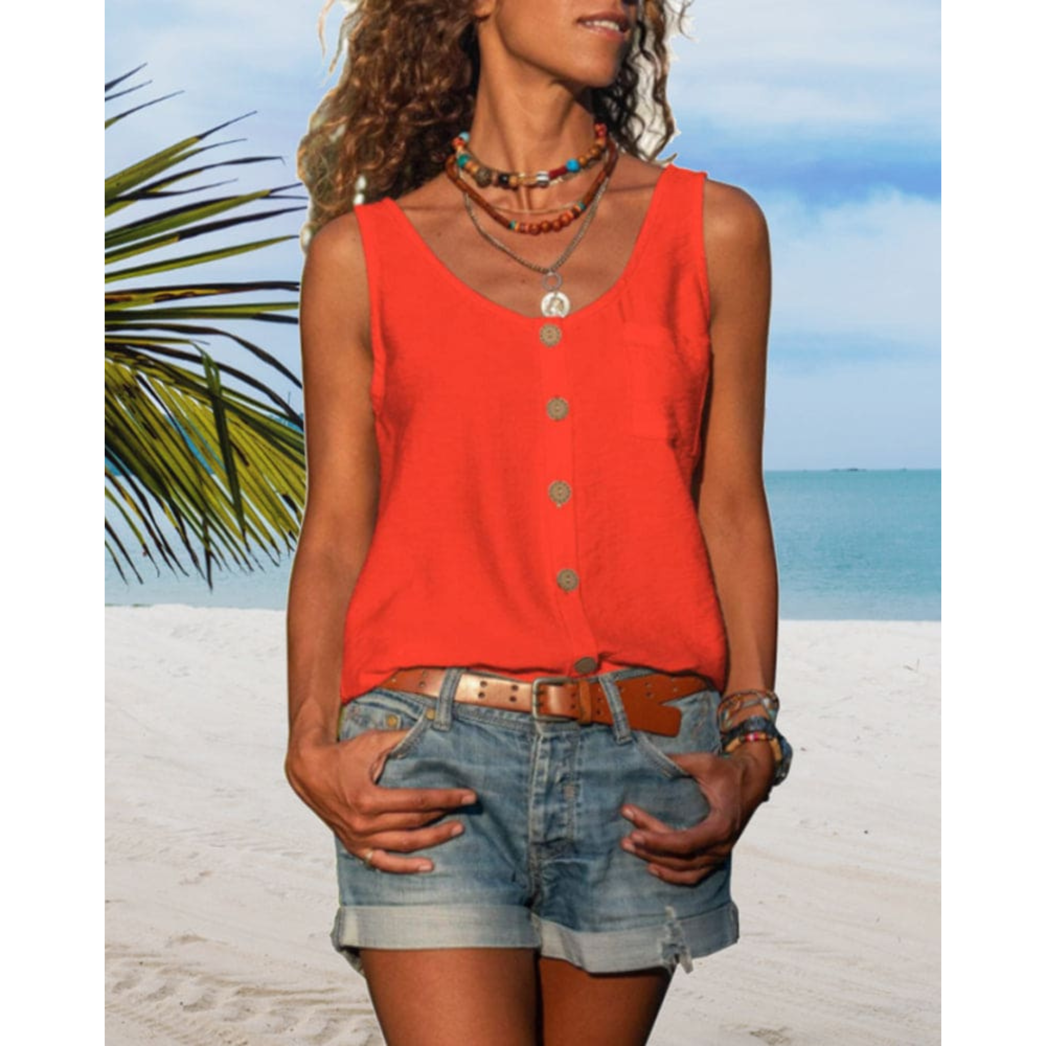 Femme en débardeur rouge et short en jean sur plage tropicale, ciel bleu, palmiers, style estival décontracté, vacances bord de mer.