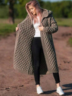 Femme portant un long manteau en tricot beige, motif torsadé, sur un chemin de terre. Mode automne, style décontracté, tendance vêtements chauds.