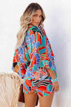 Femme portant une robe kimono colorée à motifs floraux, posant contre un mur blanc. Mode estivale, style bohème, tenue vibrante et élégante.