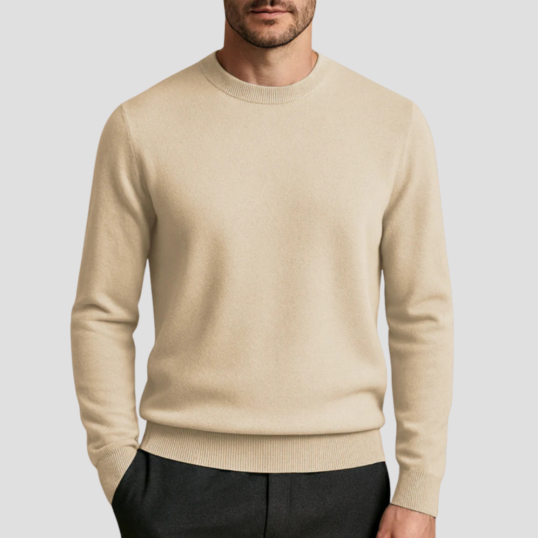 Homme portant un pull beige en laine, col rond, manches longues, avec pantalon noir. Mode masculine élégante et décontractée.