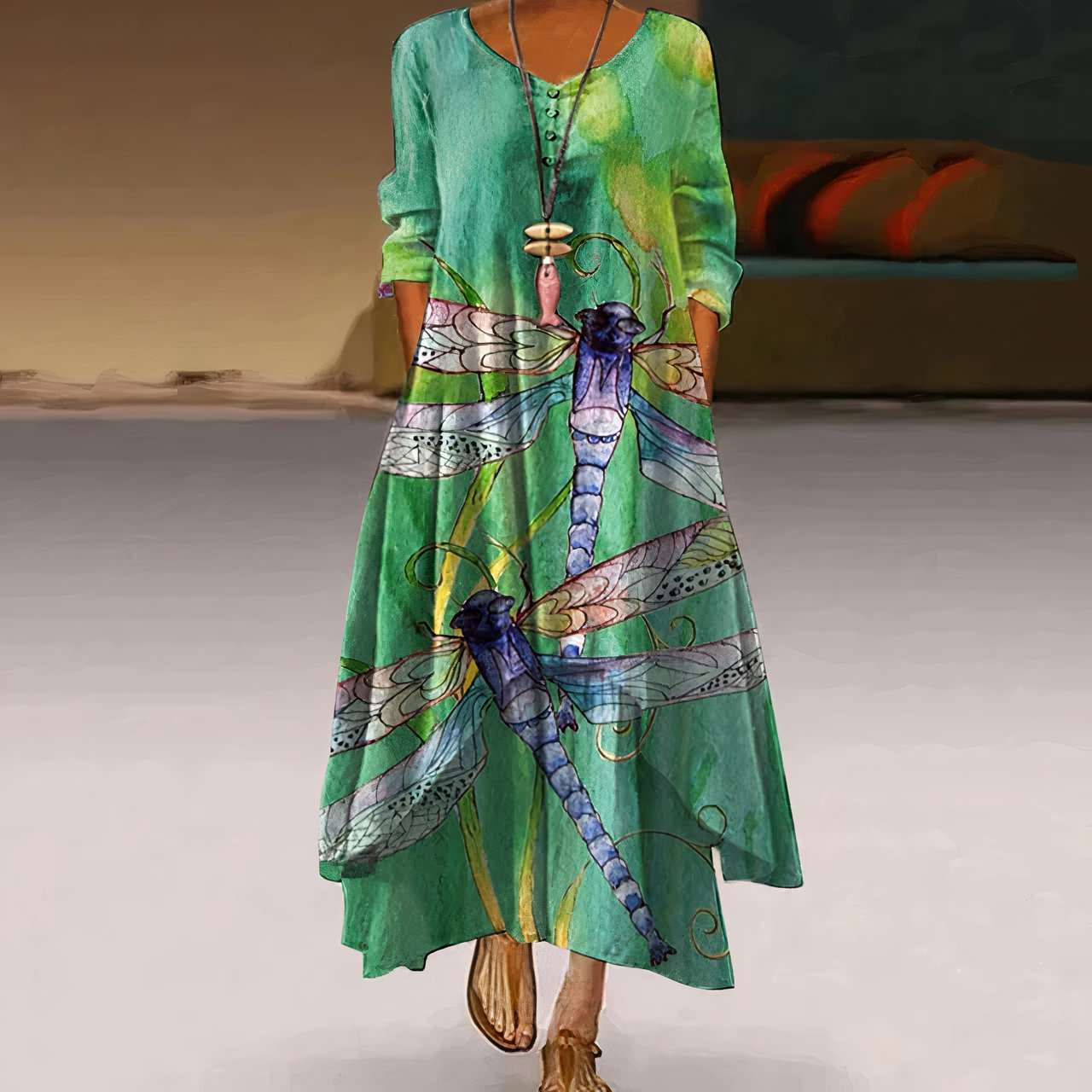 Robe longue verte avec motif libellule, manches longues, col rond, style bohème chic, femme debout, intérieur moderne, mode tendance.