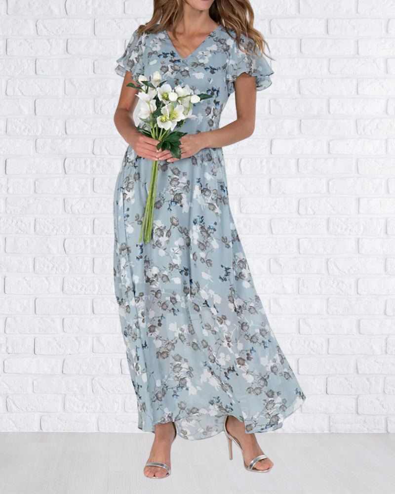 Robe longue fleurie bleue, femme tenant un bouquet de fleurs blanches, fond mur en briques blanches, mode élégante, style estival.