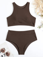 Maillot de bain deux pièces marron, style sportif, avec haut à col haut et bas taille haute. Accessoires d'été en arrière-plan.