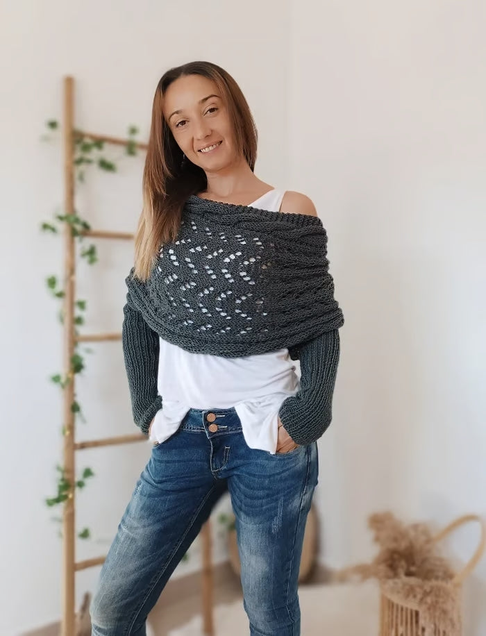 Jeune femme portant un pull tricoté gris, posant devant une échelle en bois décorée de plantes. Mode automne-hiver, style décontracté.