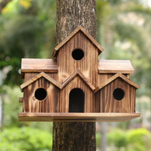 Nichoir en bois rustique fixé à un arbre, avec trois compartiments et ouvertures circulaires, dans un jardin verdoyant. Idéal pour oiseaux.