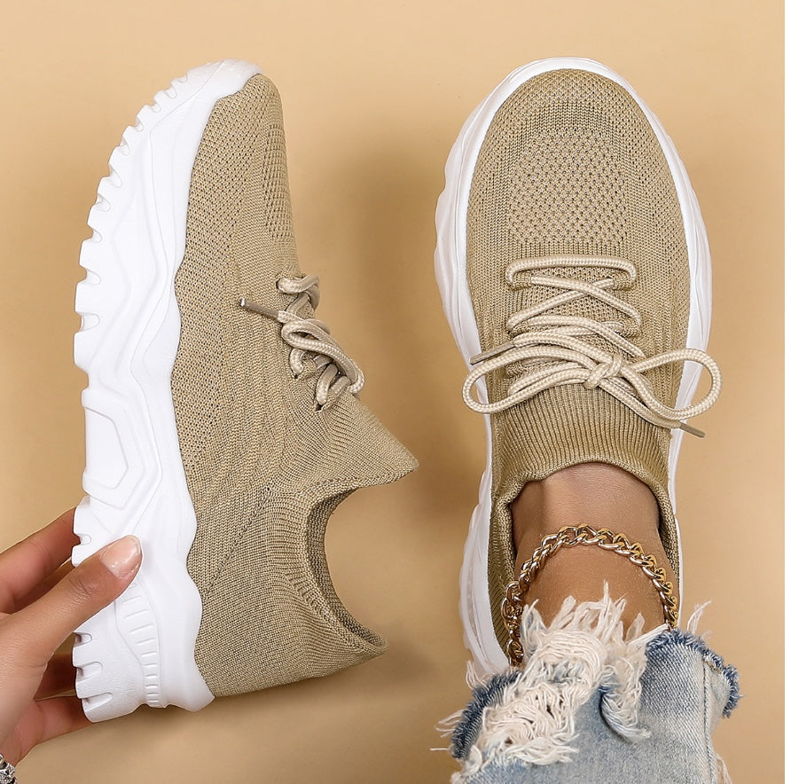 Chaussures de sport beiges en maille avec semelles blanches épaisses, portées avec un jean déchiré et bracelet doré. Mode tendance et confort.