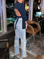 Femme portant un blazer bleu à dos ouvert et un jean délavé, debout dans un salon moderne avec vue nocturne sur la ville. Mode urbaine chic.