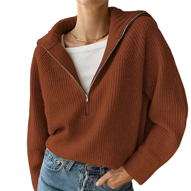 Femme portant un pull à capuche marron en tricot avec fermeture éclair, sur un t-shirt blanc, associé à un jean bleu. Mode automne-hiver tendance.